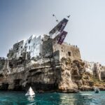 Ein Springer in der Luft von der Plattform des Red Bull Cliff Diving auf den Häusern über der Klippe von Polignano a Mare