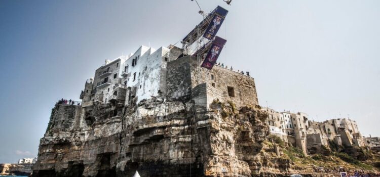 Ein Springer in der Luft von der Plattform des Red Bull Cliff Diving auf den Häusern über der Klippe von Polignano a Mare