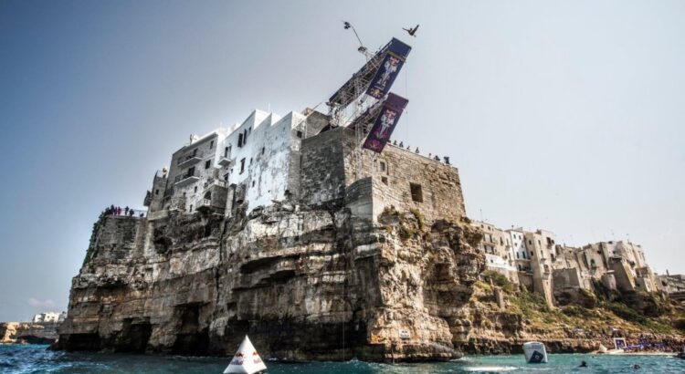 Ein Springer in der Luft von der Plattform des Red Bull Cliff Diving auf den Häusern über der Klippe von Polignano a Mare