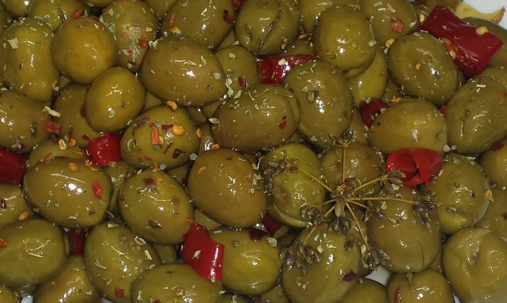 Angeschlagene grüne Oliven mit roter Chili, Oregano und Samen von wildem Fenchel