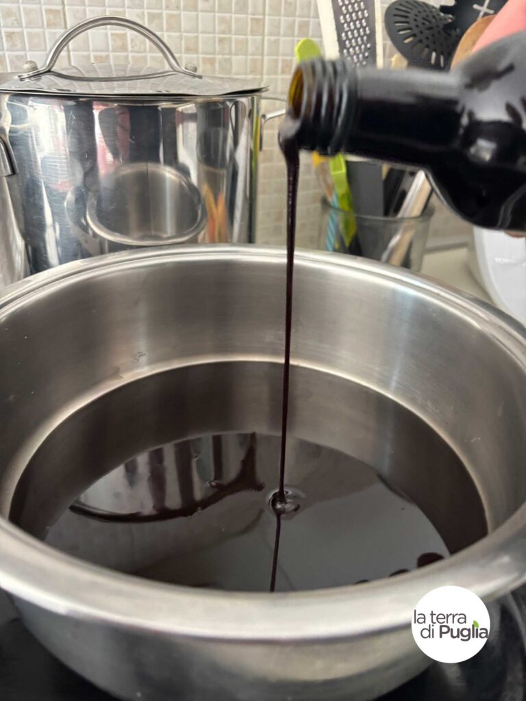 Dunkler, dickflüssiger Vincotto aus Trauben fließt aus einer Flasche in einen Edelstahltopf