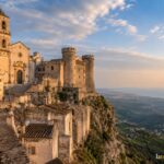 Illustration: Monte Sant'Angelo auf dem Gargano mit Kirche und Burgtürmen über dem Steilhang, im Abendlicht