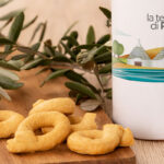 Apulische Taralli auf einem Holzbrett mit Olivenzweigen, daneben ein Ölkrug von La Terra di Puglia